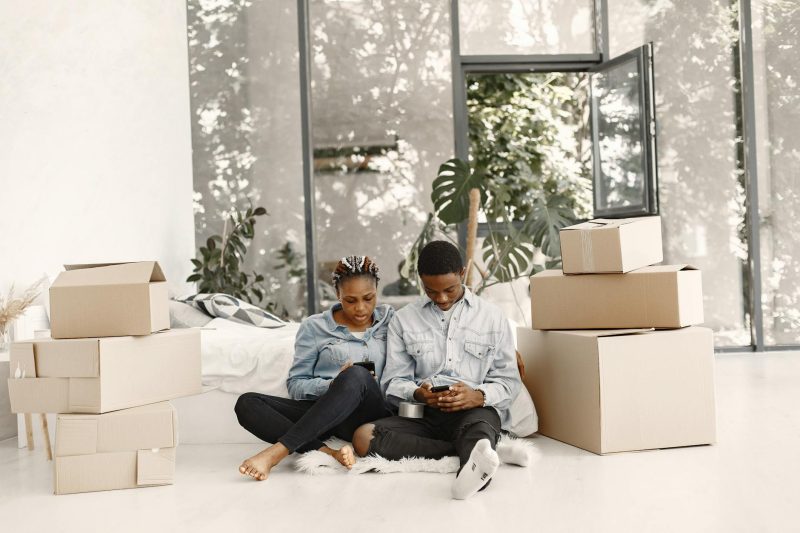 Young couple relaxing on the floor among cardboard boxes, checking their phone during a moving break.