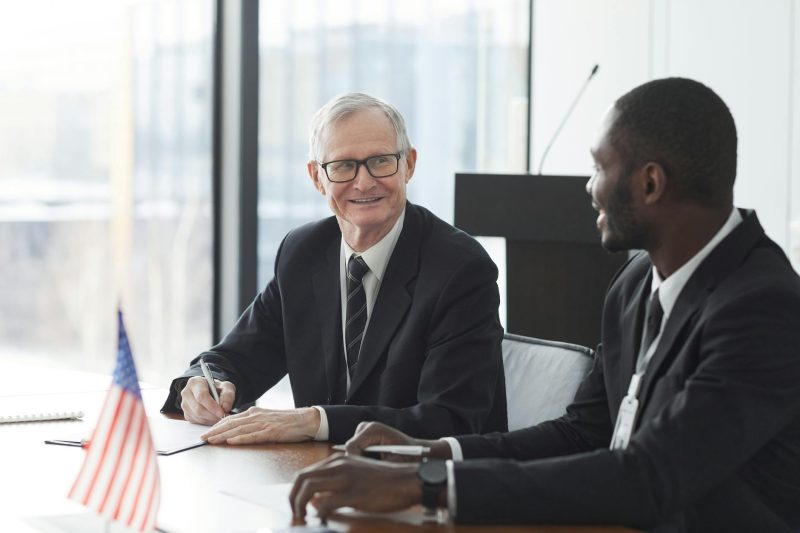 Two business professionals reviewing and signing documents at a meeting, with an American flag on the table.