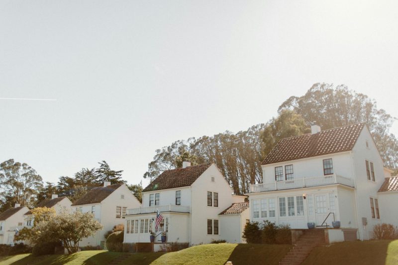 Sunlit row houses with white exteriors lining a green neighborhood in San Francisco.