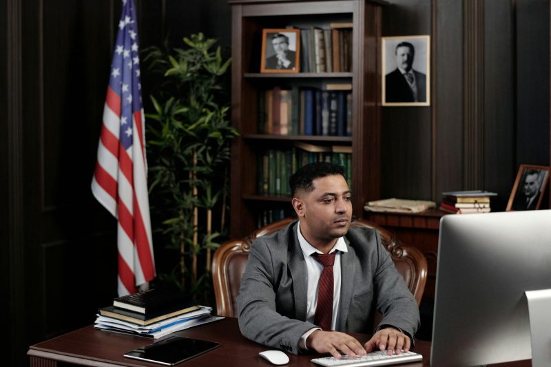 Confident businessman sitting at a desk with an American flag in his office.