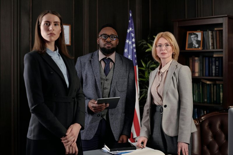 Diverse group of professionals in a formal office with bookshelves and an American flag.