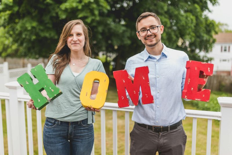 Couple smiling and holding colorful letters that spell 'HOME' in a bright, cheerful setting.