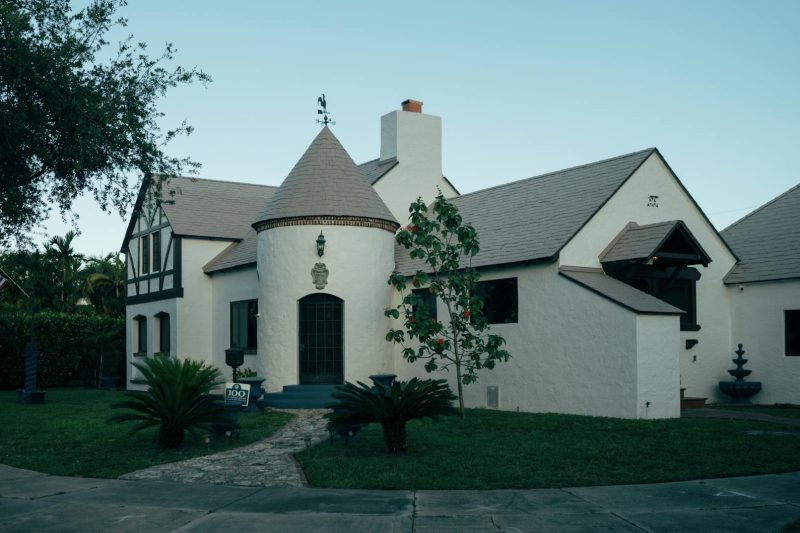 Tudor-style house with a turret surrounded by lush greenery and a vibrant garden.