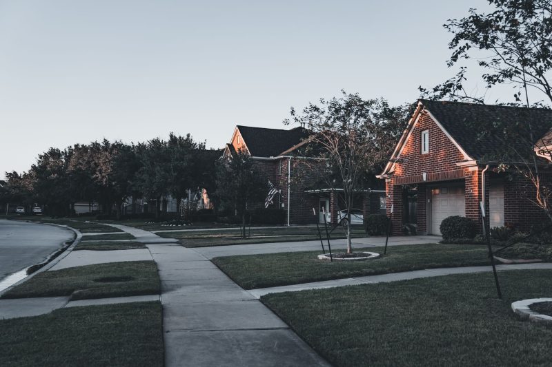 Serene suburban scene with brick houses and landscaped lawns under a dusky sky.