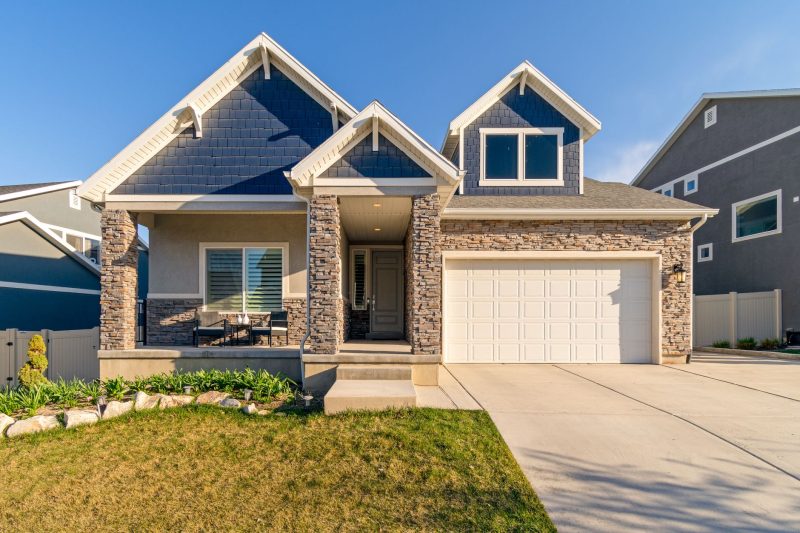Charming modern suburban home with a stone facade, surrounded by a neatly maintained lawn.