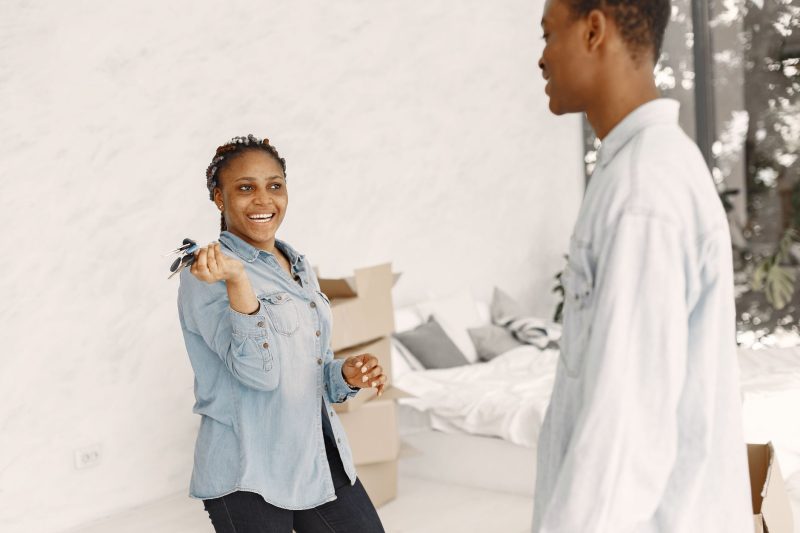Smiling couple holding house keys indoors, surrounded by boxes in a cozy home setting.