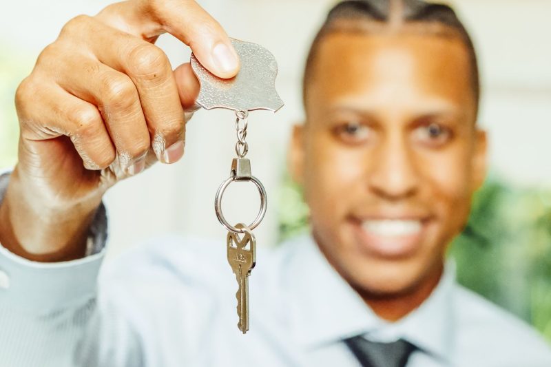 Cheerful real estate agent holding a house key, smiling in a bright indoor setting.