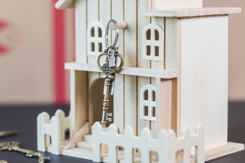 Miniature wooden house beside a vintage key, representing homeownership and real estate.
