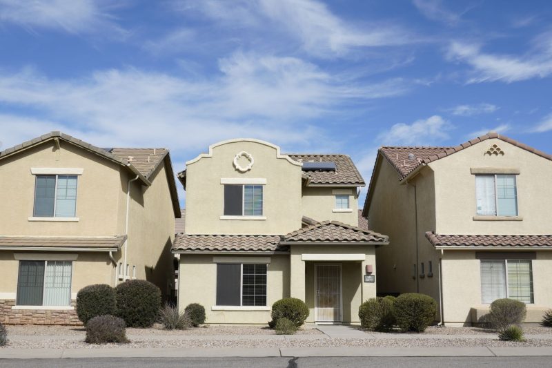 Three adjacent houses in a suburban Tucson neighborhood under a clear blue sky.