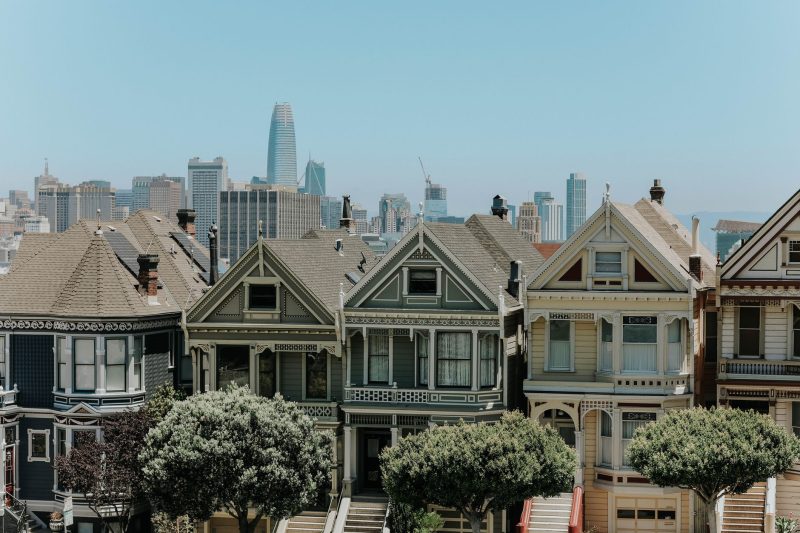 Colorful Victorian houses in San Francisco with the city skyline in the background on a clear day.