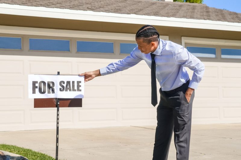 Professional real estate agent placing a for sale sign in front of a single-family home.
